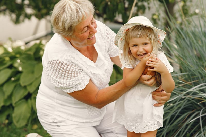A grandmother is happily playing with her granddaughter, who is holding a little chicken