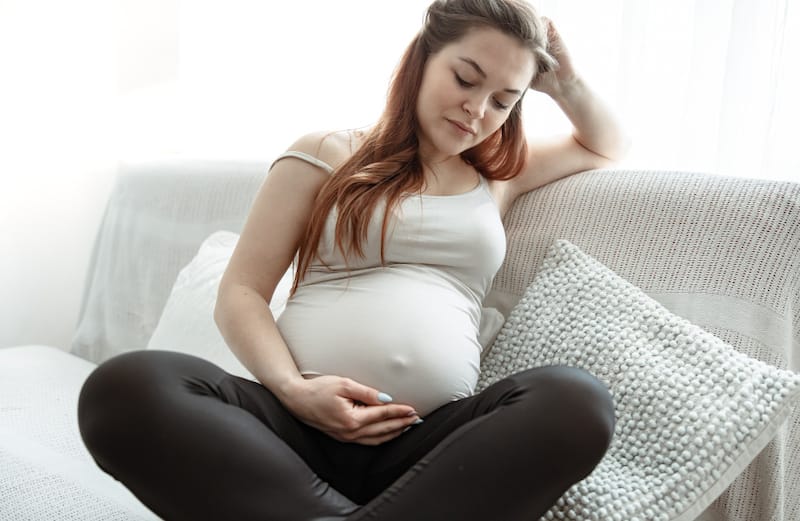 A pregnant woman is sitting down looking down at her pregnant belly