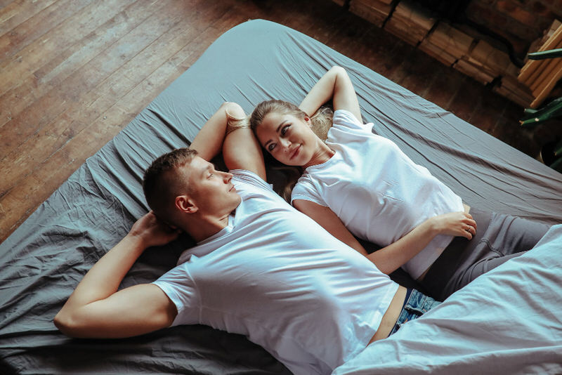 A young married couple is laying together on their bed